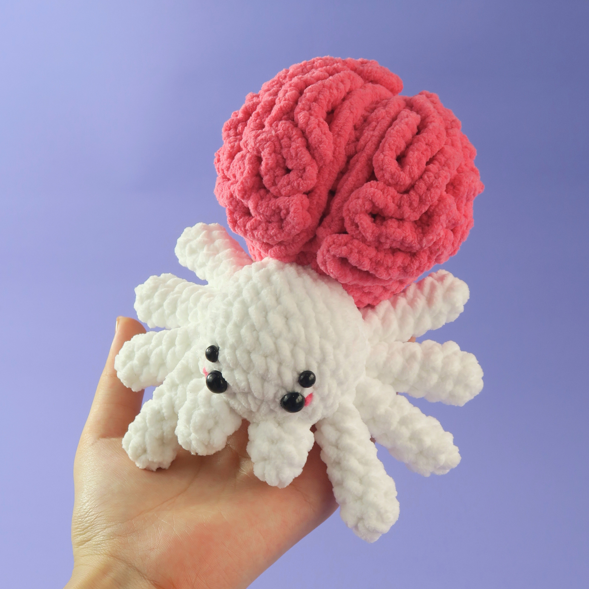 Hand holding a pink Brain Spider Crochet Pattern against a purple background