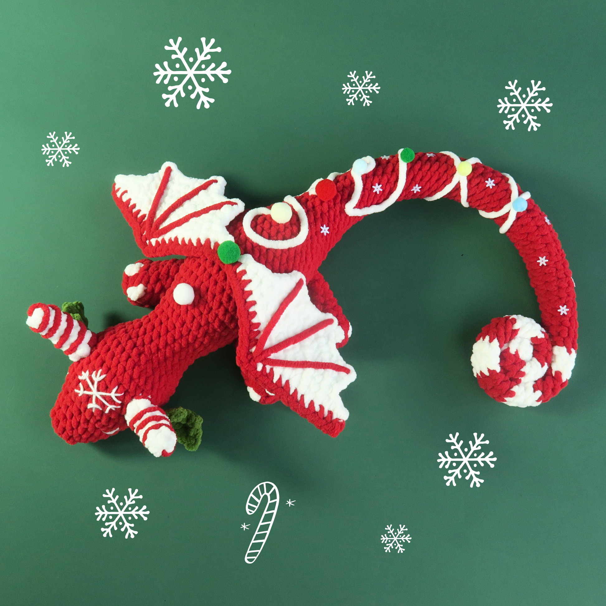 Christmas candy cane sleepy dragon crocheted on a green background with snowflakes.