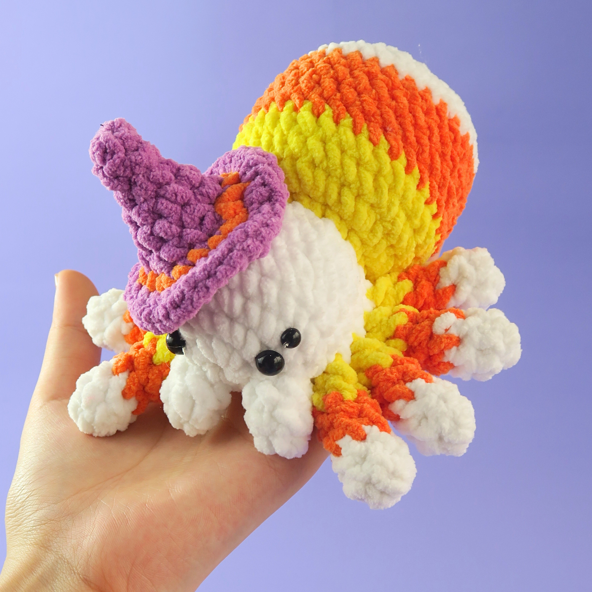 Hand holding a Candy Corn Spider Crochet Pattern with a witch hat against a purple background