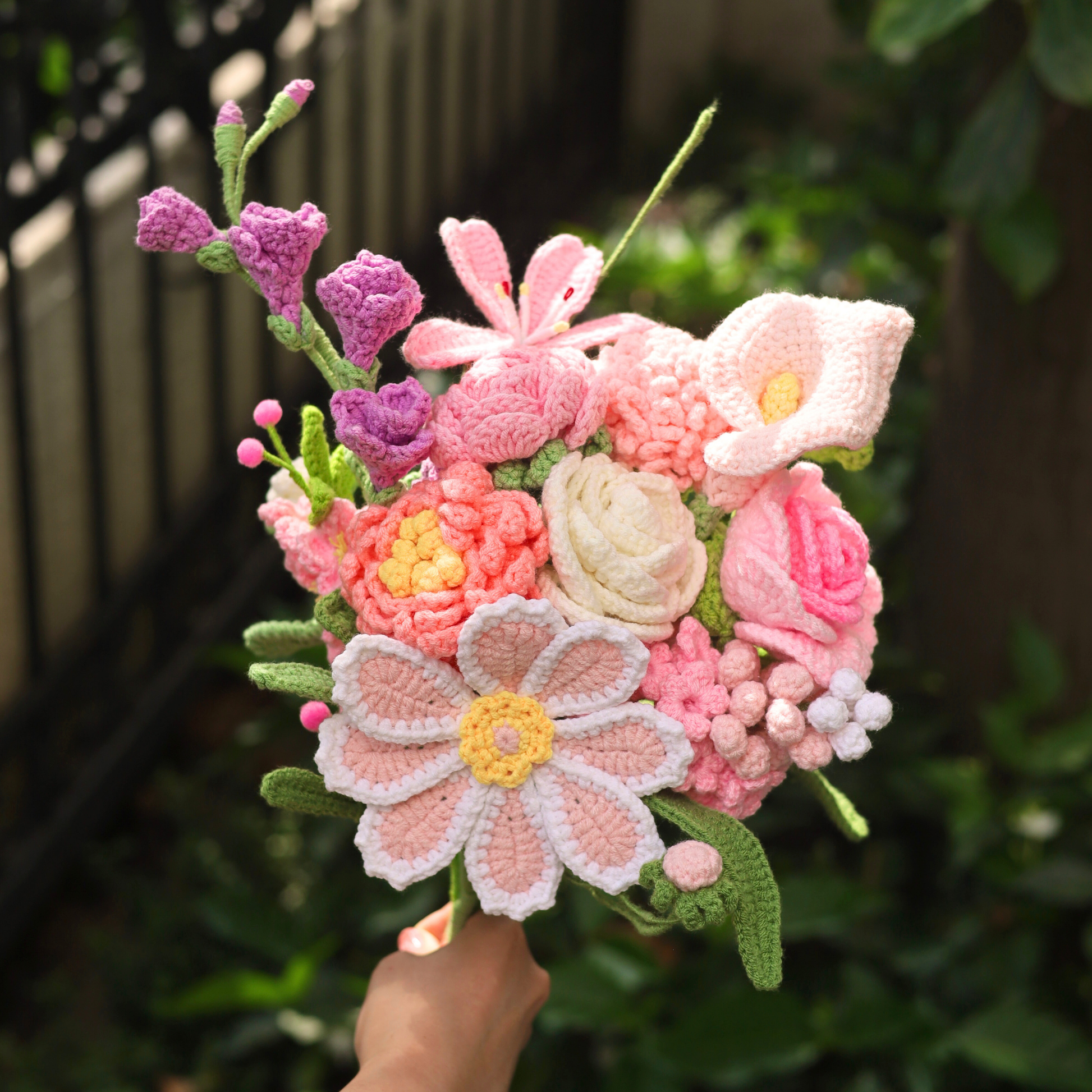 Handmade crochet flower bouquet with pink, white, and green colors against a blurred natural background.