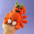 Hand holding Pumpkin Spider Crochet Pattern against a purple background