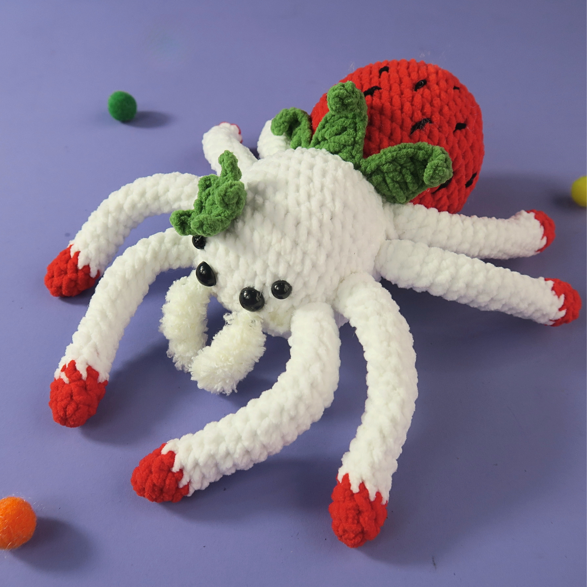 White strawberry crochet spider with red legs and green eyes on a purple background