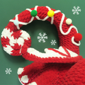 Crocheted candy cane with red, white, and green colors on a green background with snowflake decorations.