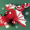 Red and white crocheted christmas candy cane dragon toy on a green background with snowflakes.