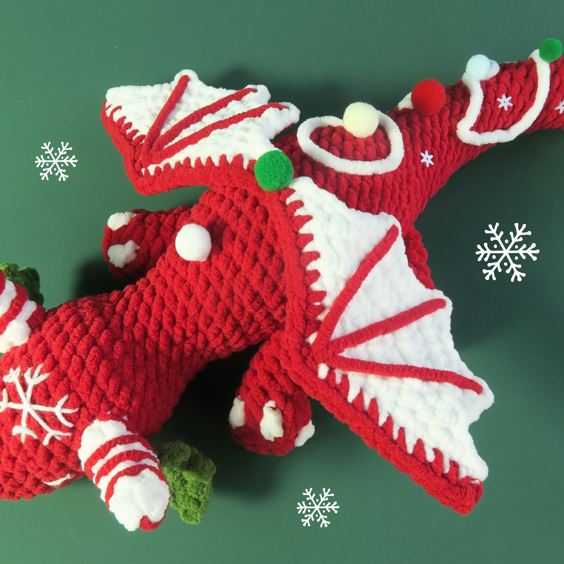 Red and white crocheted christmas candy cane dragon toy on a green background with snowflakes.